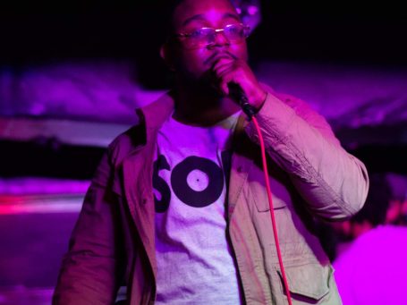 Lance Greenwood performing on stage, wearing glasses and a shirt with the word "SOUL."